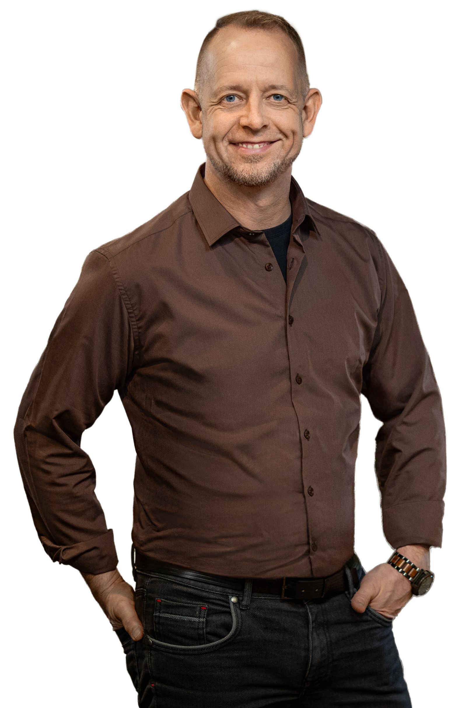 Lächelnder Mann im braunen Hemd und Jeans, Hände in den Hosentaschen.